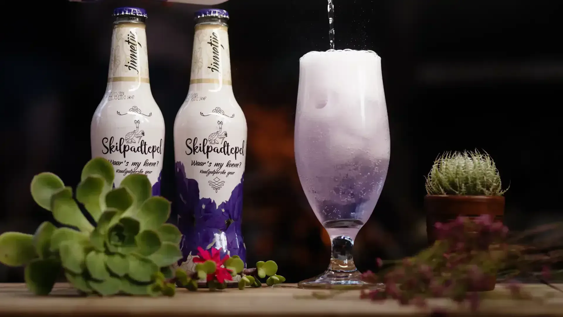 Twee wit Kaalgatperske Jinnetjie-bottels en 'n sprankelende pers drank wat oor ys in 'n tulpglas giet