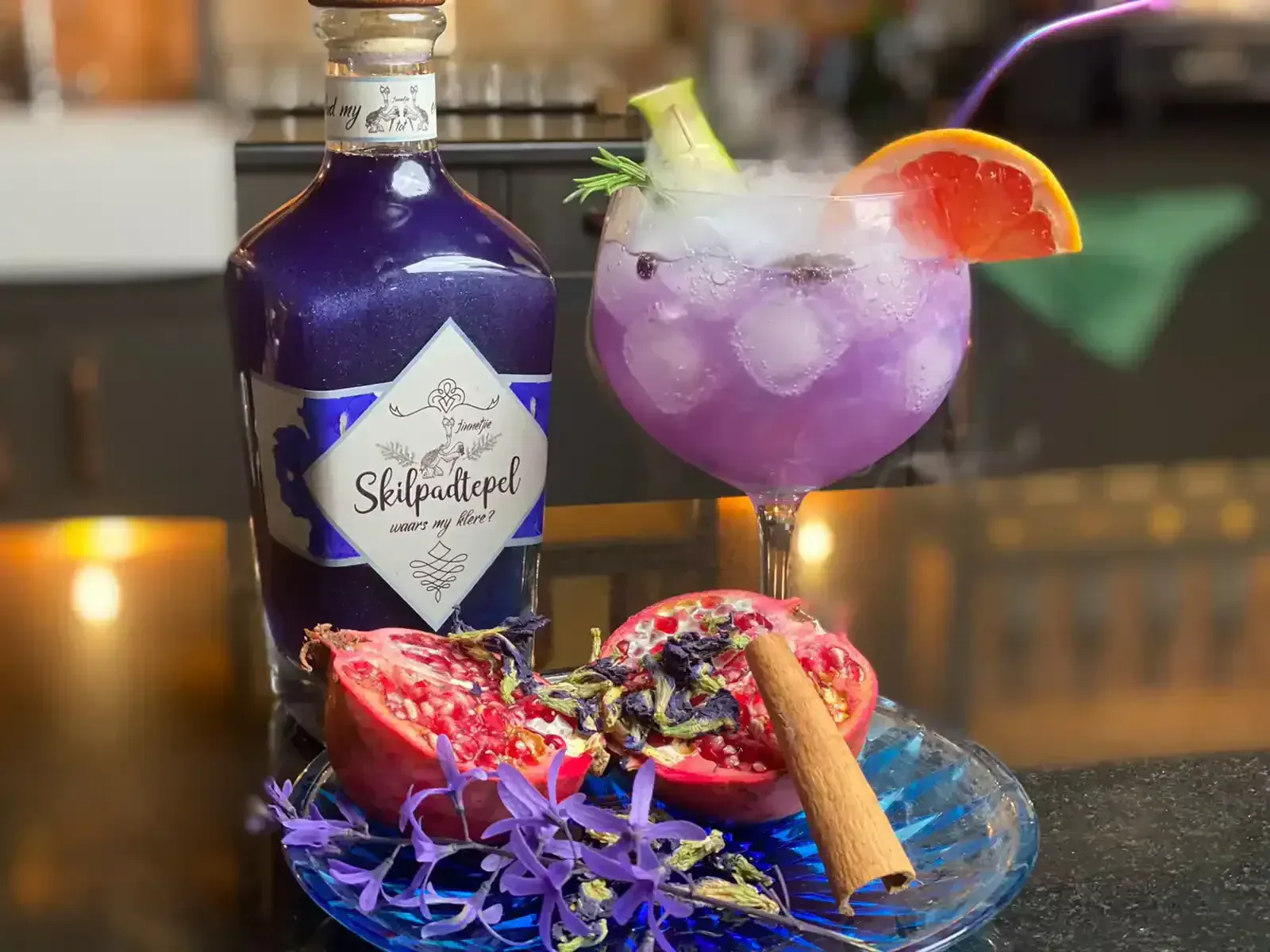 Skilpadtepel jenewer en 'n gemengde skemerkelkies met granaatappel, kaneel en pers blomme op 'n blou borde