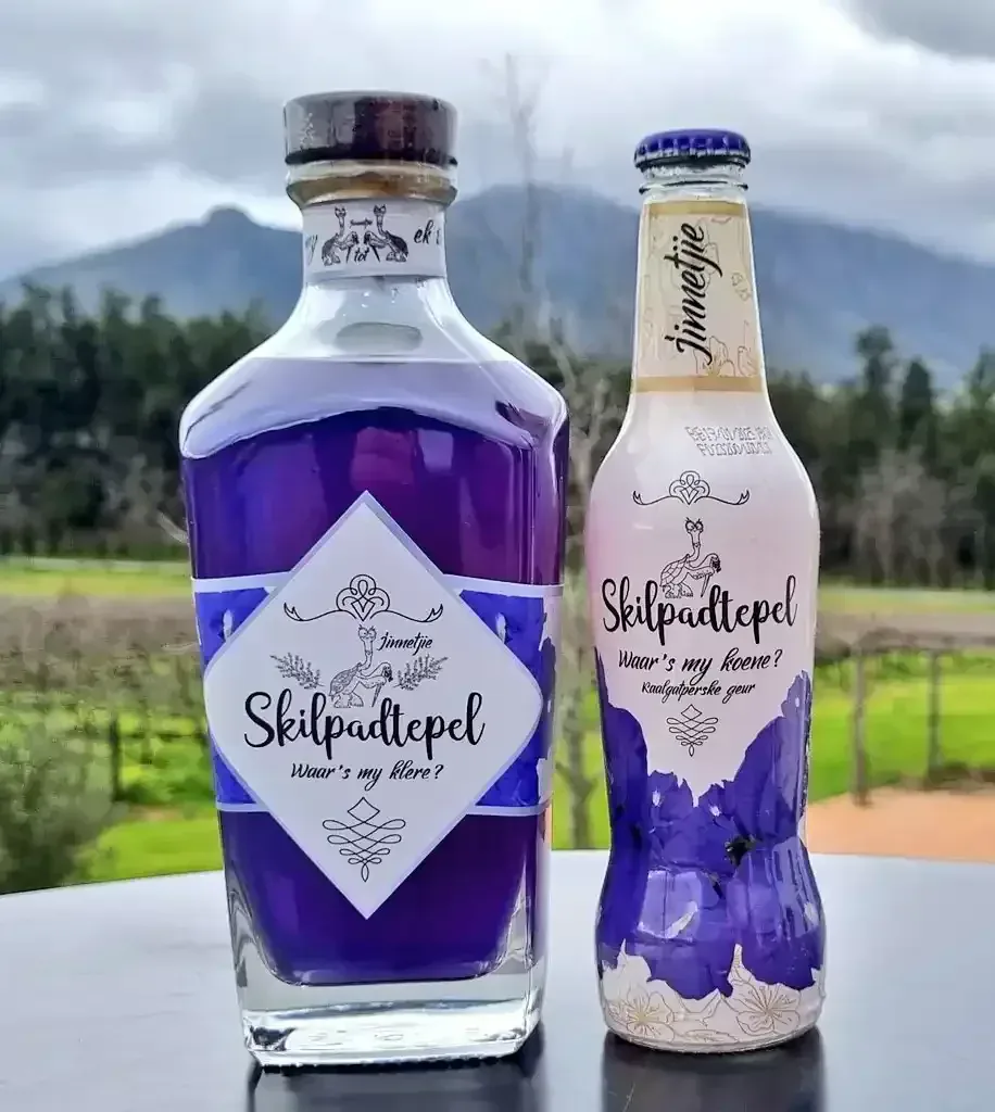 Skilpadtepel jenewer en Kaalgatperske spirituskoeler bottels teen 'n wingerd en bergagtige landskap