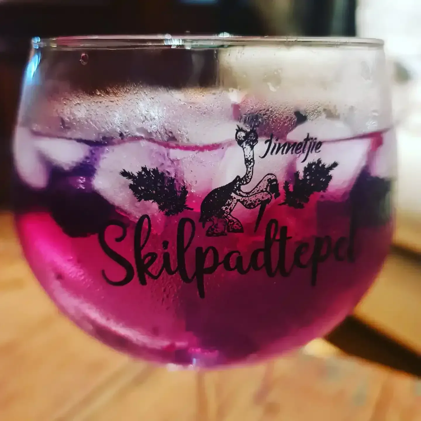 Koue pienk skemerkelkies met bessies en ys in 'n Skilpadtepel-ballonglas met volstruis-illustrasie